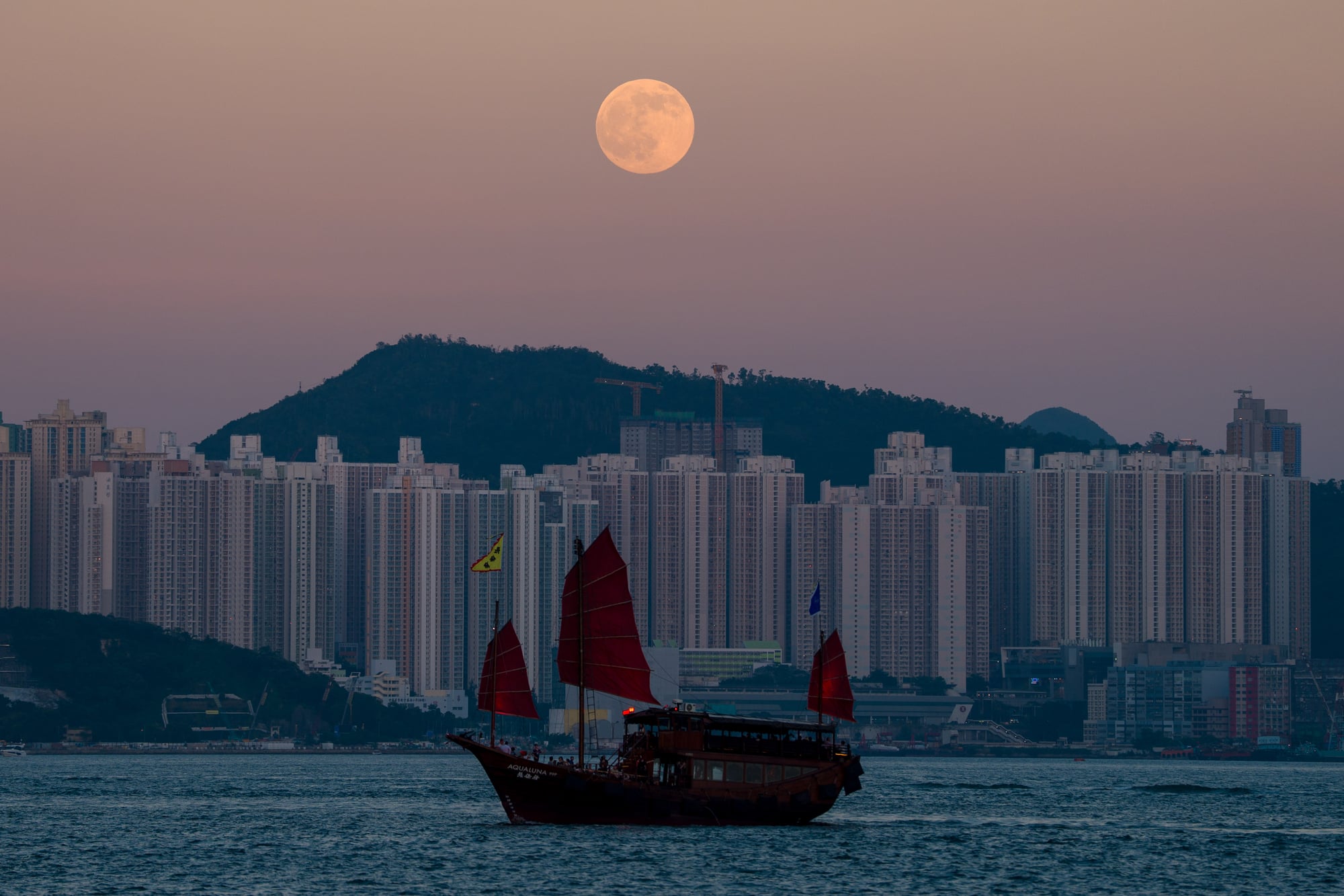 A Junk boat sailing in Victoria harbor in front of a rising moon