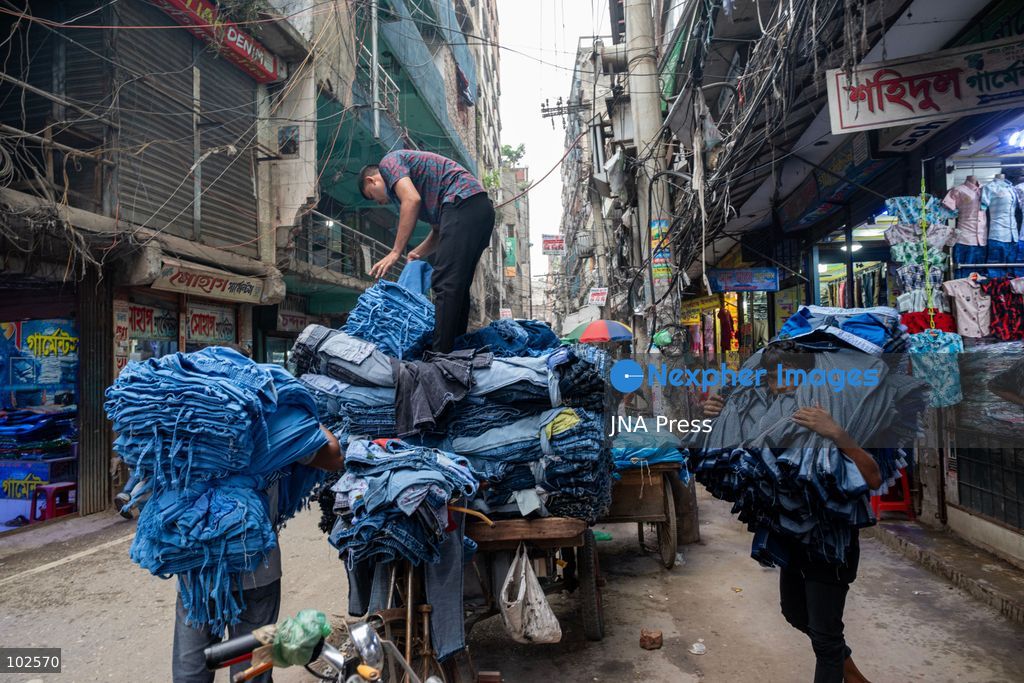 KALIGANJ, DHAKA, BANGLADESH, OCTOBER 7, 2026: Garment traders and workers transport large bundles of denim clothing through a busy market in Kaliganj, Dhaka. Jeans and other garments are stacked outside shops and moved through crowded streets by handcart, bicycle and truck for distribution and sale. The market forms part of the local apparel trade, where workers and traders handle large volumes of clothing moving between wholesalers, retailers and buyers. Photo by Bipul Ahmed / JNA Press. (Photo by Bipul Ahmed/JNA Press via Nexpher Images)
