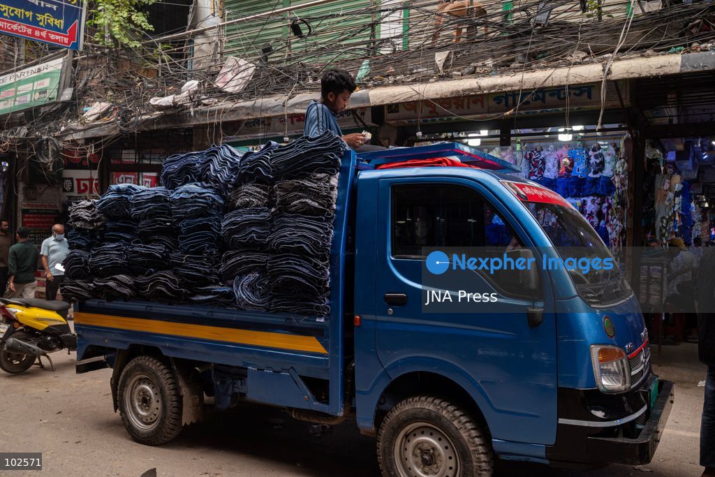 KALIGANJ, DHAKA, BANGLADESH, OCTOBER 7, 2026: Garment traders and workers transport large bundles of denim clothing through a busy market in Kaliganj, Dhaka. Jeans and other garments are stacked outside shops and moved through crowded streets by handcart, bicycle and truck for distribution and sale. The market forms part of the local apparel trade, where workers and traders handle large volumes of clothing moving between wholesalers, retailers and buyers. Photo by Bipul Ahmed / JNA Press. (Photo by Bipul Ahmed/JNA Press via Nexpher Images)
