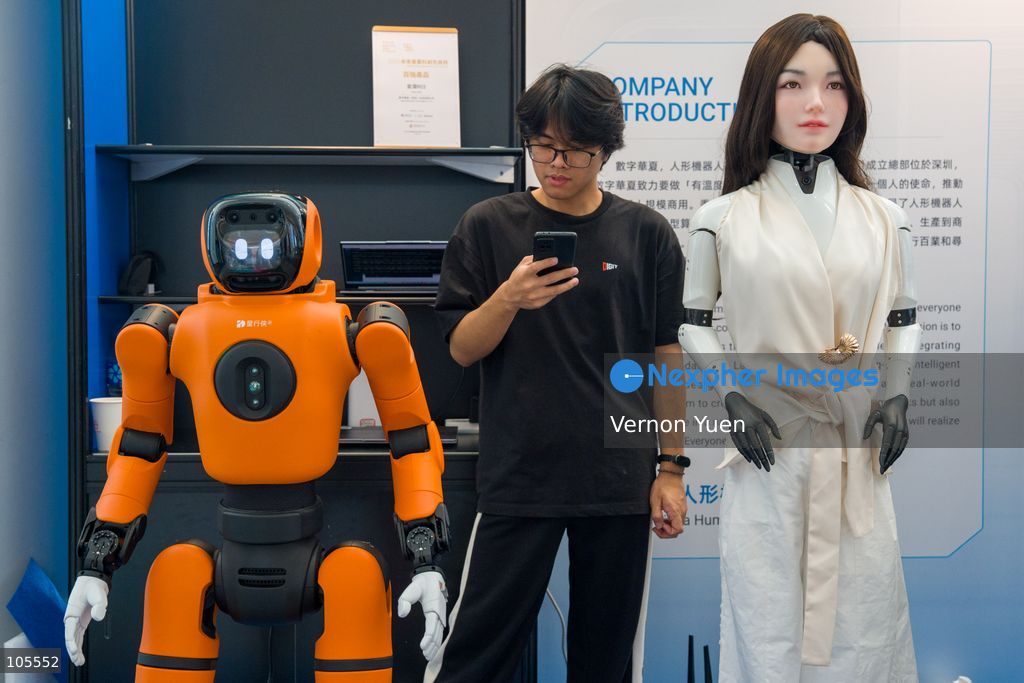 A man looking at his phone standing between two robots at the Hong Kong Electronics Fair on October 14, 2026 in Hong Kong. (Photo by Vernon Yuen/Nexpher Images)