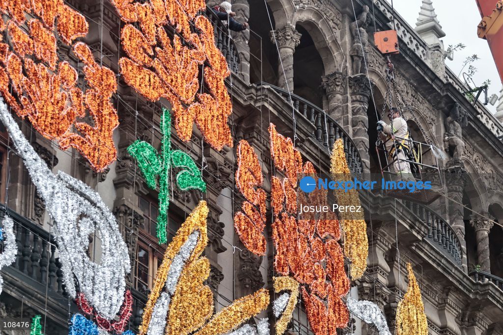 A worker is lifted in a crane to install and secure the lighting for the Day of the Dead on October 22, 2026, in Mexico City, Mexico. Construction crews working for the Mexico City government have begun assembling and installing the structures that will illuminate the buildings surrounding the city’s Zócalo. Using cranes, cables, and various framework components, they are preparing everything for the unveiling of the Monumental Ofrenda (altar), which will feature the world’s tallest Catrina, so that both locals and tourists can enjoy the start of the Day of the Dead celebrations in Mexico. (Photo by Josue Perez/Nexpher Images)
