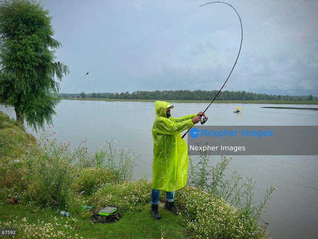 An angler clad in a raincoat braves rainfall to fish along the banks of Wular Lake on July 21, 2026 in Sopore, India. (Photo by Nexpher Images/Nexpher Images)