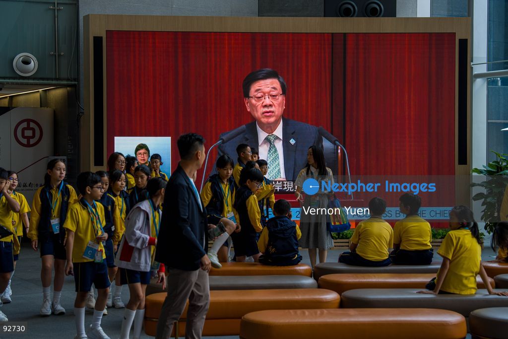 People walking pass a screen showing Hong Kong Chief Executive John Lee speaking at the legislative council as he delivers his 2026 policy address and the first Hong Mong Five Year plan on September 16, 2026 in Hong Kong. Hong Kong today released its First five year plan along side with the Chief Executive’s 2026 Policy Address. (Photo by Vernon Yuen/Nexpher Images)