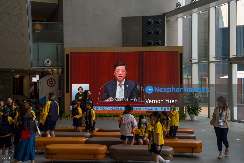 People walking pass a screen showing Hong Kong Chief Executive John Lee speaking at the legislative council as he delivers his 2026 policy address and the first Hong Mong Five Year plan on September 16, 2026 in Hong Kong. Hong Kong today released its First five year plan along side with the Chief Executive’s 2026 Policy Address. (Photo by Vernon Yuen/Nexpher Images)