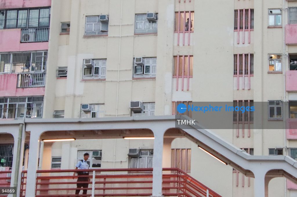 A wide view shows uniformed police officers on high security alert on a nearby footbridge while a television cameraman films the funeral procession area from a residential corridor of Model Housing Estate overlooking the Hong Kong Funeral Home during the wake for Tung Chee-hwa on September 19, 2026 in Hong Kong. (Photo by Gordon Choi/TMHK via Nexpher Images)