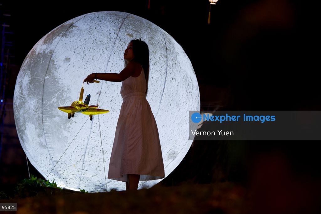 A woman holding an airplane shaped lantern standing in front of an inflatable moon at the Mid autumn festival lights at Shek O on September 23, 2026 in Hong Kong. (Photo by Vernon Yuen/Nexpher Images)