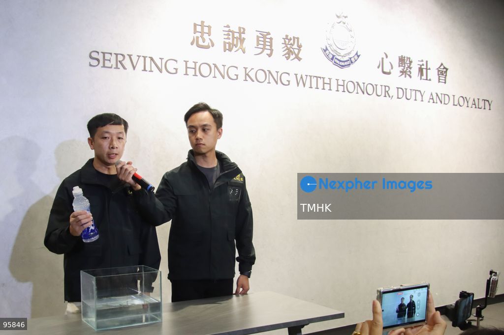 Police officers immerse a bottled drink into a container of water behind microphones during a press briefing on September 23, 2026 in Hong Kong. Police demonstrated how meltwater accumulates in the gap behind the packaging label during ice chilling, explaining the liquid released when squeezed is not leaked content. (Photo by Gordon Choi/TMHK via Nexpher Images)