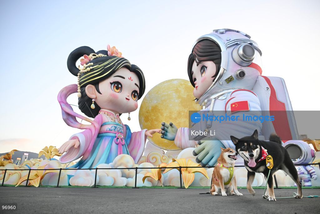 Two dogs posing photo in front of large illuminated figures depicting a traditional Hanfu and an astronaut are displayed during a nighttime event in Hung Hom New Waterfront, the day after the Mid-Autumn Festival on September 26, 2026 in Hong Kong. (Photo by Kobe Li/Nexpher Images)