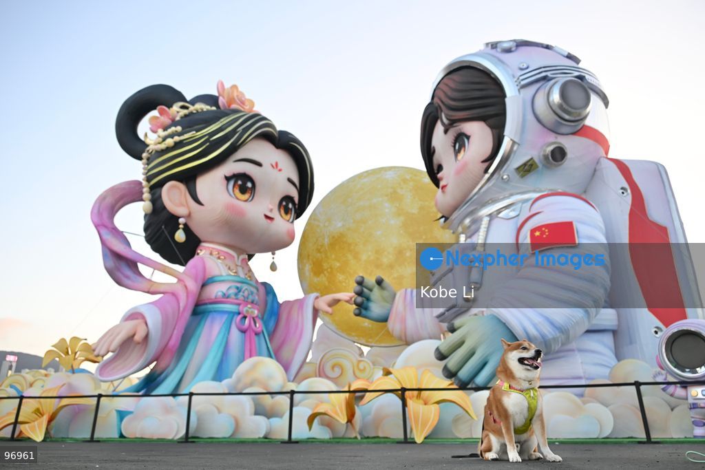 A dog posing photo in front of large illuminated figures depicting a traditional Hanfu and an astronaut are displayed during a nighttime event in Hung Hom New Waterfront, the day after the Mid-Autumn Festival on September 26, 2026 in Hong Kong. (Photo by Kobe Li/Nexpher Images)