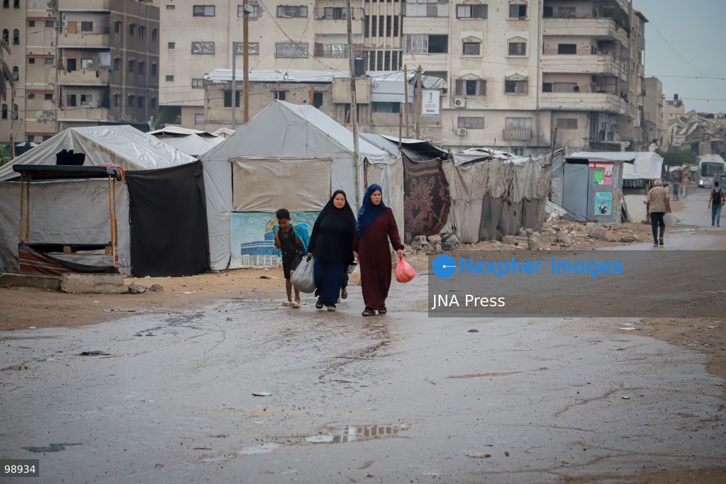 GAZA CITY, GAZA STRIP, SEPTEMBER 29, 2026: Palestinians walk through rain-soaked streets surrounded by destroyed buildings and tents sheltering displaced families in Gaza City. The arrival of rainy weather is adding to difficult living conditions for displaced Palestinians, many of whom remain in tents and makeshift shelters with limited protection from the elements. Photo by Mohammed M. Skaik / JNA Press. (Photo by Mohammed M Skaik/JNA Press via Nexpher Images)