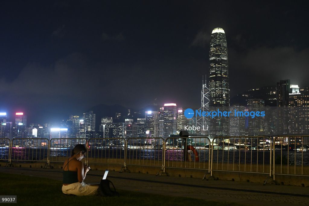 A person sits on a grassy area near a railing, looking out at the illuminated skyline of Hong Kong at night on September 29, 2026 in Hong Kong. (Photo by Kobe Li/Nexpher Images)