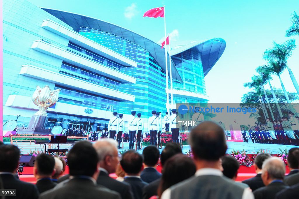Attendees pause to watch a live broadcast of the flag-raising ceremony at Golden Bauhinia Square displayed on a giant LED screen inside the foyer of the Hong Kong Convention and Exhibition Centre on October 1, 2026 in Hong Kong. (Photo by Zulu Lo/TMHK via Nexpher Images)
