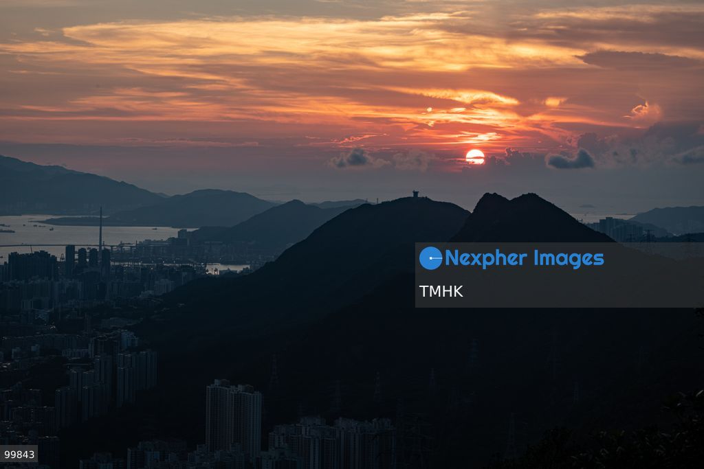A general view captured from Kowloon Peak (Fei Ngo Shan) shows the sun setting toward Stonecutters Island and the western approaches of Victoria Harbour on October 1, 2026 in Hong Kong, casting vivid golden and orange dusk hues across the Stonecutters Bridge and maritime shipping channels ahead of the National Day fireworks. (Photo by Kevin Li/TMHK via Nexpher Images)